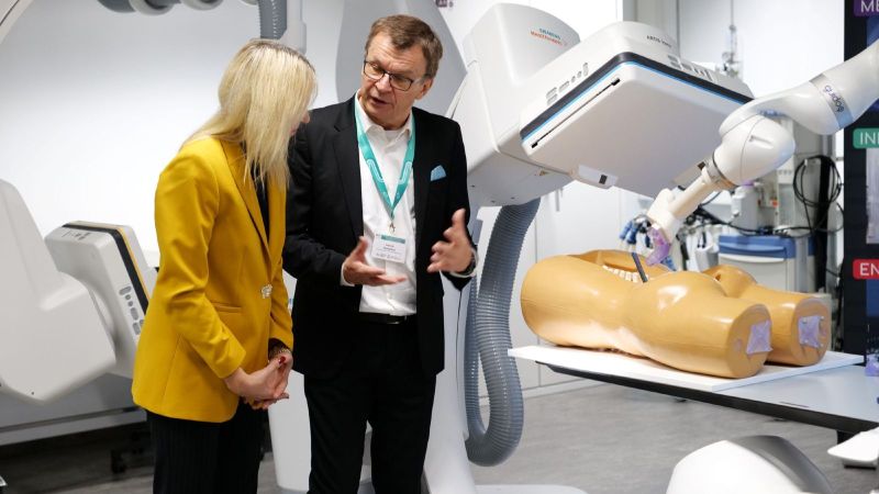 Die Staatsekretärin sieht sich den Roboterarm an und hört der Erklärung zu.