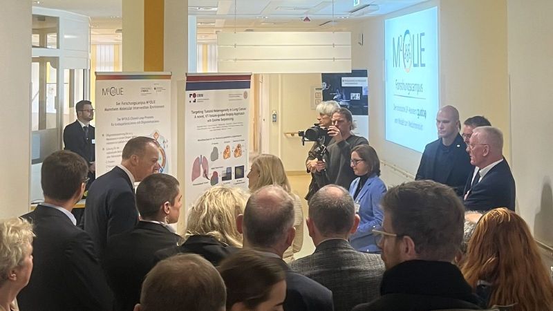 Die Bundesgesundheitsministerin schaut sich Plakate an, die die Arbeit von M²olie präsentieren. Sie ist umringt von Menschen, die sie dabei begleiten.