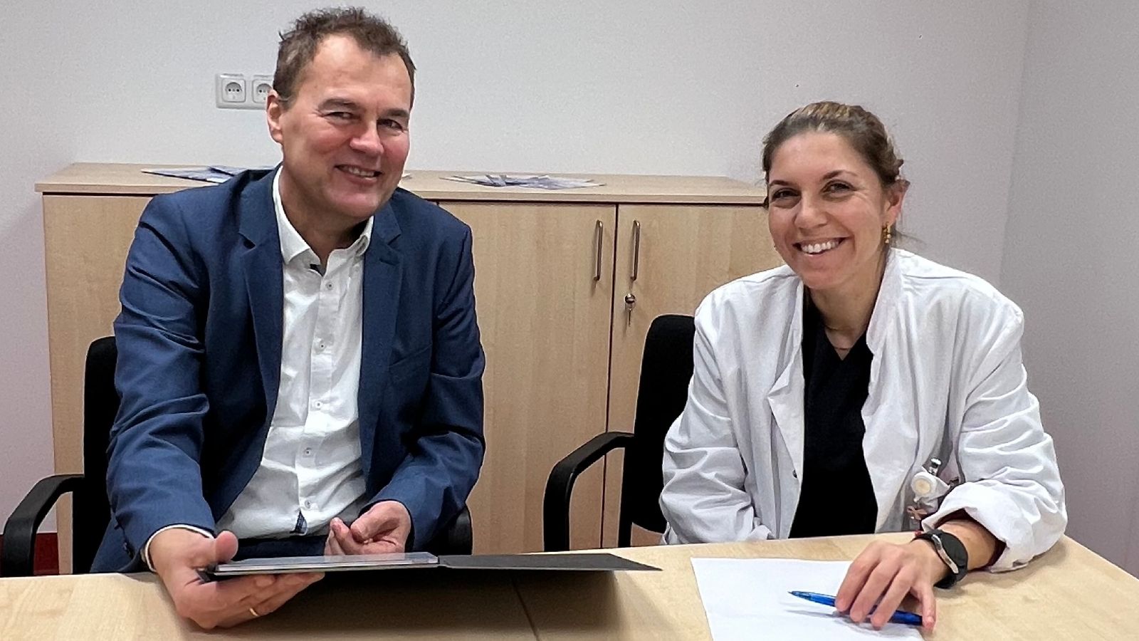 Egbert Janssen und Anna Simeonova-Chergou sitzen am Tisch. Vor sich ein Laptop und ein Notizblock, im Hintergrund ein Sideboard.
