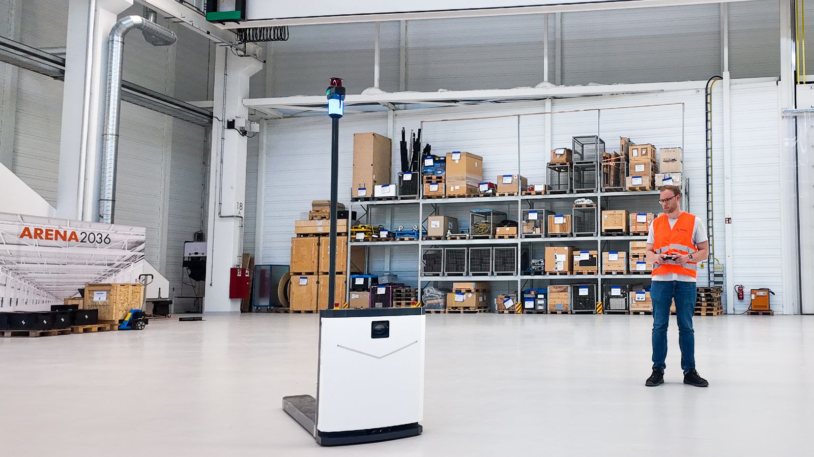 Ein Mitarbeiter steuert einen Roboter von NODE Robotics in einer groß wirkenden recht leeren Halle.