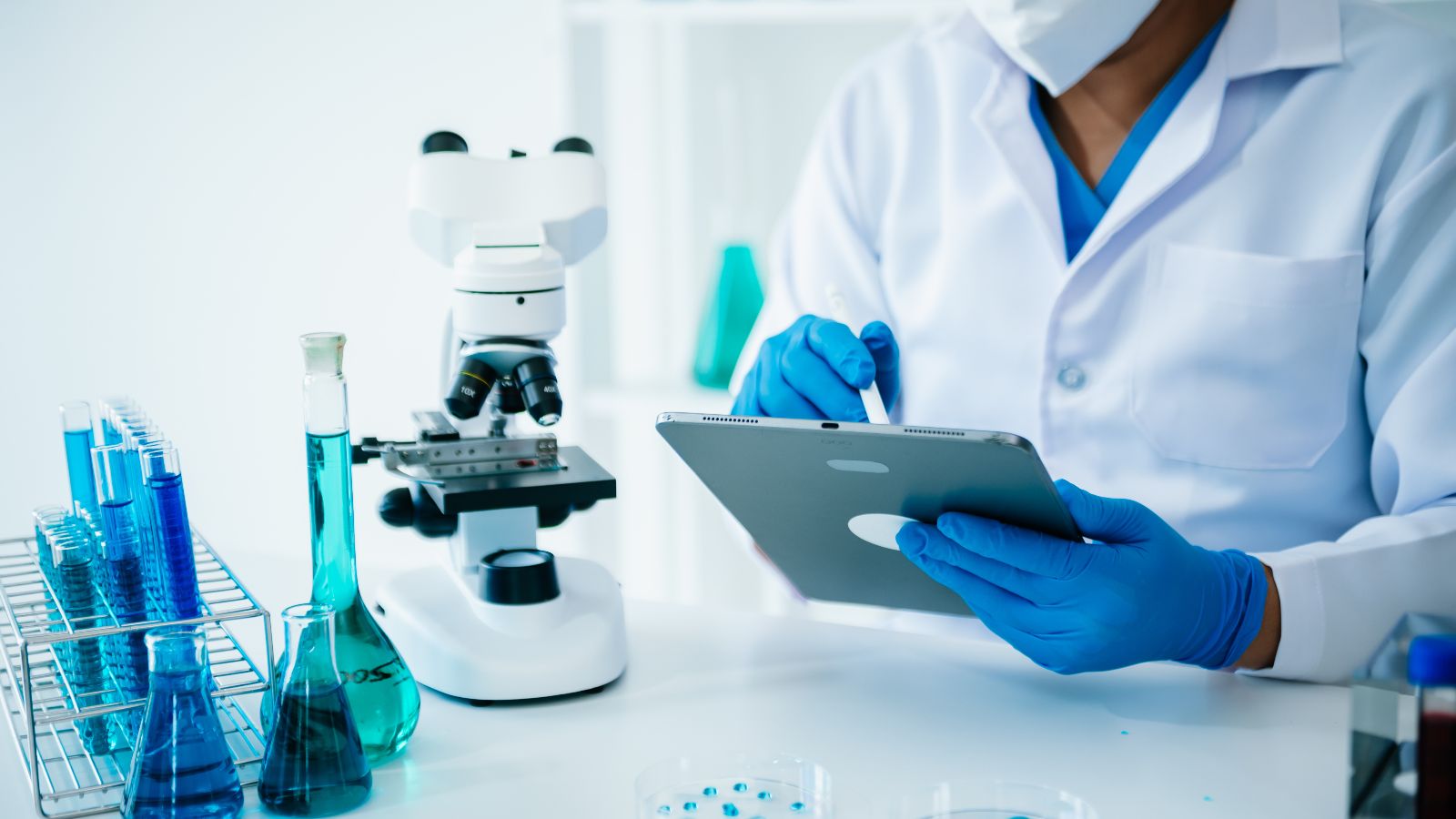 Mikroskop, Flüssigkeiten und eher im Hintergrund Laborant am Tablet